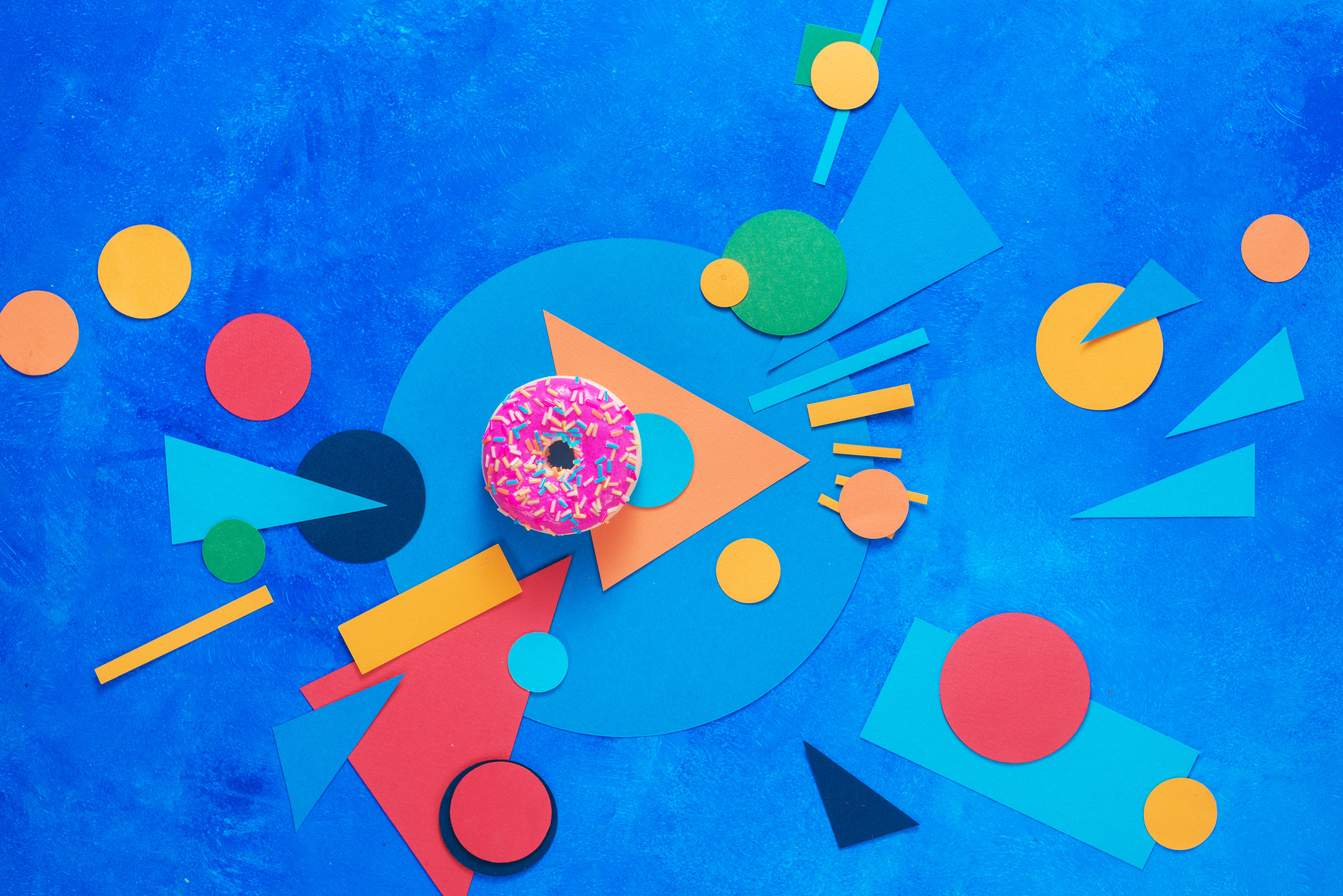 A pink donut with colorful paper decorations. Color blocking flat lay with sweets. Complementary colors concept with copy space.
